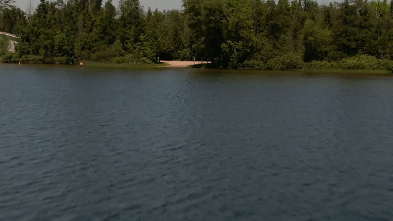 Aerial shot skimming low across a lake toward a wooded boat launch