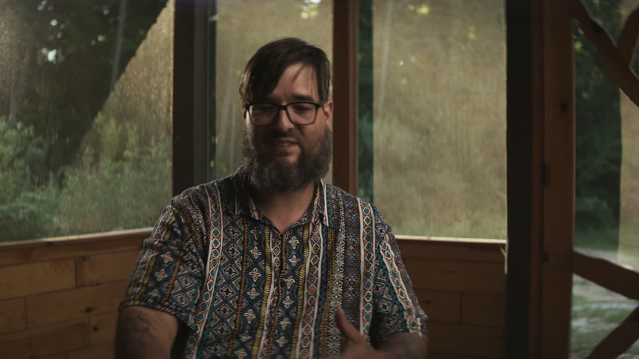 Eric Molitor speaks during a filmed interview on a screened porch in evening light